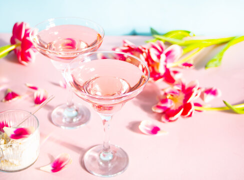 Glasses of pink cocktail with flowers and petals. Birthday party or Valentines day romatic couple date concept.