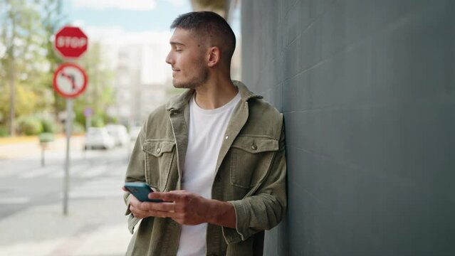 Young hispanic man smiling confident using smartphone at street