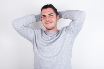 Young handsome dark haired man wearing fitted T-shirt over white wall stretching arms, relaxed position.