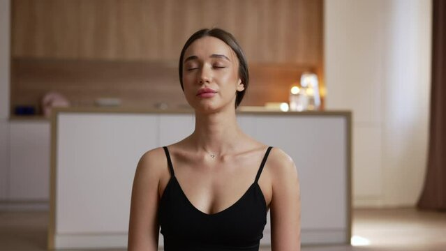 Portrait of young disabled woman is meditating and sitting on floor in home interior spbas. 4k Close view of beautiful Caucasian female closes her eyes and breathes deeply, does asana on mat and