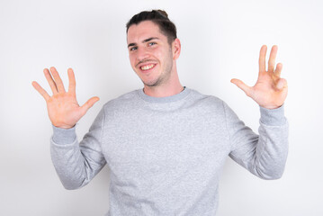 Young handsome dark haired man wearing fitted T-shirt over white wall showing and pointing up with fingers number nine while smiling confident and happy.