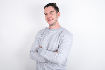 Young handsome dark haired man wearing fitted T-shirt over white wall  happy face smiling with crossed arms looking at the camera. Positive person.
