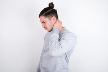 Young handsome dark haired man wearing fitted T-shirt over white wall Suffering of neck ache injury, touching neck with hand, muscular pain