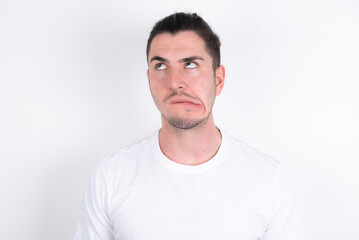 Young handsome dark haired man wearing fitted T-shirt over white wall making grimace and crazy...