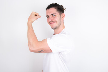 Portrait of powerful cheerful Young handsome dark haired man wearing fitted T-shirt over white wall...