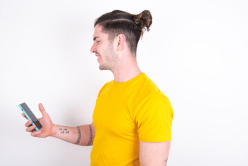 Rear view photo portrait of Young caucasian man wearing yellow t-shirt over white background using smartphone smiling