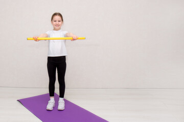 little girl stands on a gymnastic mat and holds a gymnastic stick with her arms outstretched in...