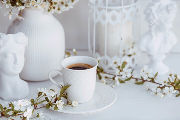Obraz na płótnie Canvas A beautiful postcard. A white coffee cup with a saucer, a statuette, candles and a vase with a bouquet of cherry blossoms. Beautiful still life. Spring time. The concept of 