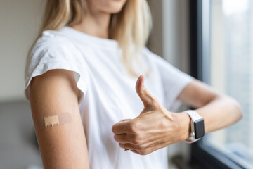 Happy young caucasian woman with blonde hair in white t-shirt showing patch on arm, feeling good after anti coronavirus covid-19 injection, recommending healthcare vaccination, medical insurance