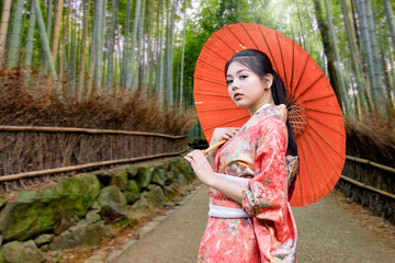 A woman in a kimmono dress holds an umbrella in a bamboo grove in Japan. Major tourist attractions in Japan