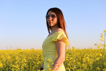 Happy woman turned away back, walks run along yellow field rapeseed, hands raised to side enjoys...