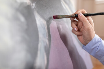Close-up of the hand of a artist woman holding a paintbrush while finishing one of her works.