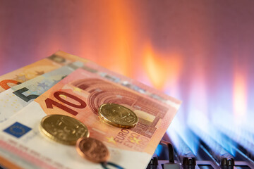 Euro banknotes and coins are lying next to a burning gas burner. The concept is to increase the cost of supplying and paying for natural gas. The energy crisis. High cost, gas price.