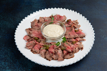 Beef slices and sauce in a plate on a dark background.
