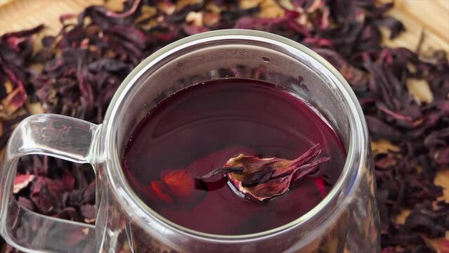 Red tea in a glass cup on a white background. Red hibiscus tea is poured into a transparent glass with double walls. A cup of tea rotating on a wooden board.