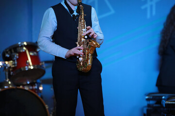 A musician a music college student playing solo saxophone stands on stage at the drums in a blue...