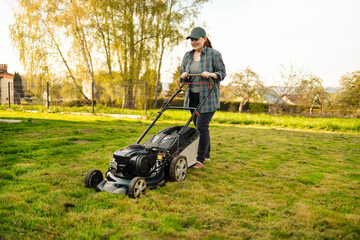 30s woman mows the lawn with an electric lawn mower at countryside.