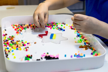 A child plays a thermo mosaic. A boy playing at a white table