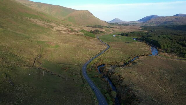 A car driving in a country side winding road near the Glenlosh Valley in county Galway, Ireland, with mountains in the background