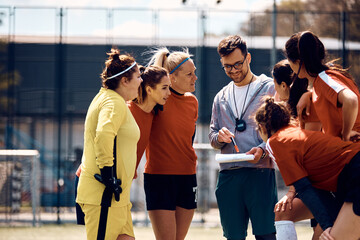 Female players and their coach going through game strategy before soccer match on playing field.