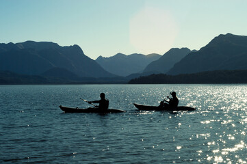 Blue silhouette of a mountain range with reflection of the sun in the waters of a lake people riding in kayaks. lifestyle concept