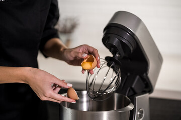 hands of a cook near a food processor break an egg