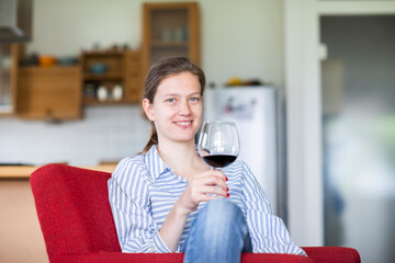 Junge blonde Frau zu Hause entspannt mit einem Glas Rotwein au fem Sofa