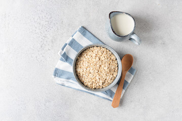 Oat flakes, rolled oats in bowl and jug of milk. Concept of healthy food. Grey concrete table...
