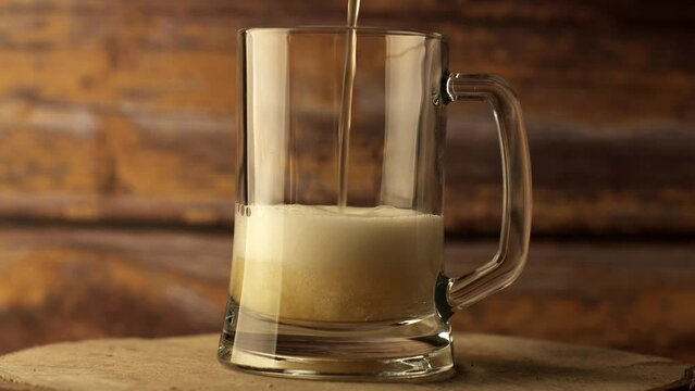 Beer is poured into a beer glass, a lot of bubbles and foam. Warm wooden background