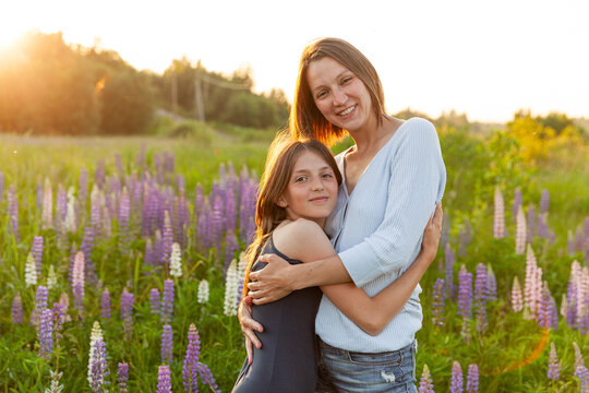 Young mother embracing her child outdoor. Woman and teenage girl on summer field with blooming wild flowers green background. Happy family mom and daughter playing on meadow
