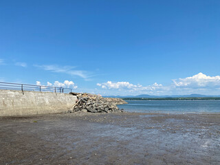 Plage à marée basse avec une jetée de pierres dans un port. Paysage en bord de mer, ciel bleu en été.