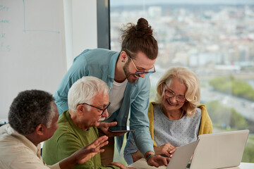 A young educator holding tablet and showing to multicultural group of senior students how to do web design.