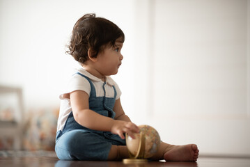 Cute little baby boy toddler sitting on wooden floor playing with globe ball while looking away and...