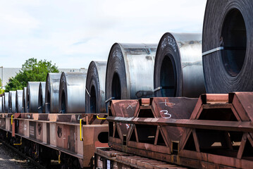 Large rolls of sheet metal lying on a freight wagon pulled by locomotives.
