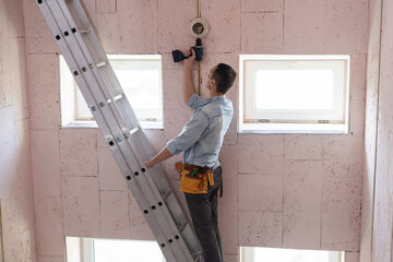 An electrician fixing wires, installing light on the ceiling