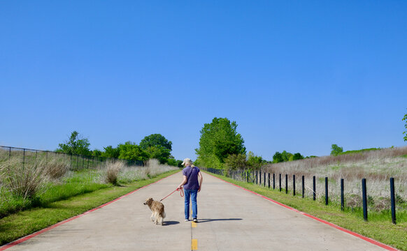 A Woman Walking Her Dog Along A Trail In The Great Trinity Forest, An Expansive Urban Park Within Dallas, Texas.