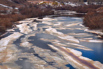 Melting ice on a river in a hilly area with trees. spring landscape