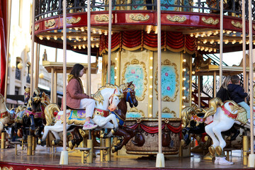 a little girl riding on animals on roundabout carousel in amusement park. child having fun on family weekend or vacations.