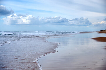 Landscape of a very long sandy beach with a blue sky full of clouds. Horizontal photography.