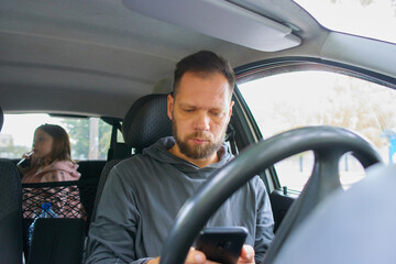a bearded man with a phone in a car with his little daughter