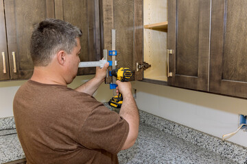 Male carpenter drilling in door cabinet with kitchen furniture handle