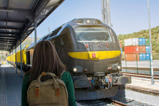 Rear view of a woman traveling with a backpack  at a train station. Travel Concept. Image with copy space. 