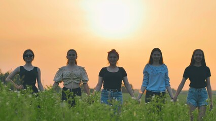 Fototapeta premium Girls stand holding hands at sunset on a summer evening.