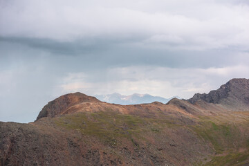 Dramatic aerial landscape with sunlit mountain top during rain at changeable weather. Atmospheric mountain scenery with sharp rocks in sunlight under lead gray cloudy sky. Rainy clouds in mountains.