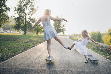 Stylish crazy European hipster mom with tattoos with daughter child and dog Australian Shepherd breed riding On skateboards and pavement in park, warm summer evening and family time and hobbies © natalialeb