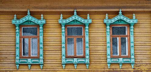 Three old windows with carved wooden architraves on shabby board wall. - obrazy, fototapety, plakaty
