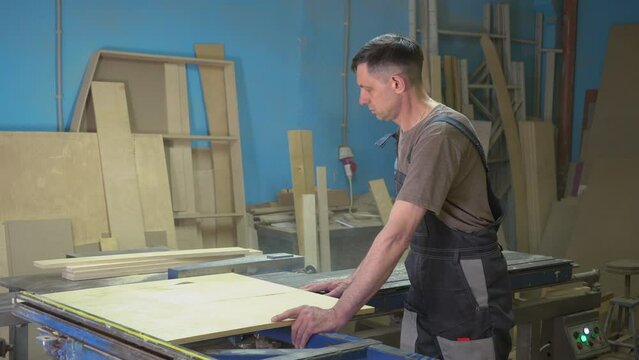 A carpenter cuts wood on a circular saw in a joinery. Furniture manufacture.