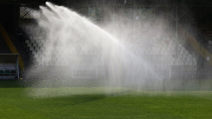 Podlewanie trawy w czasie słonecznej suszy na boisku sportowym.