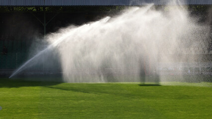 Podlewanie trawy w czasie słonecznej suszy na boisku sportowym. - obrazy, fototapety, plakaty