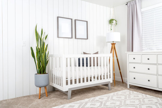 A modern farmhouse baby nursery bedroom with blank mock-up picture frames on the wall. 